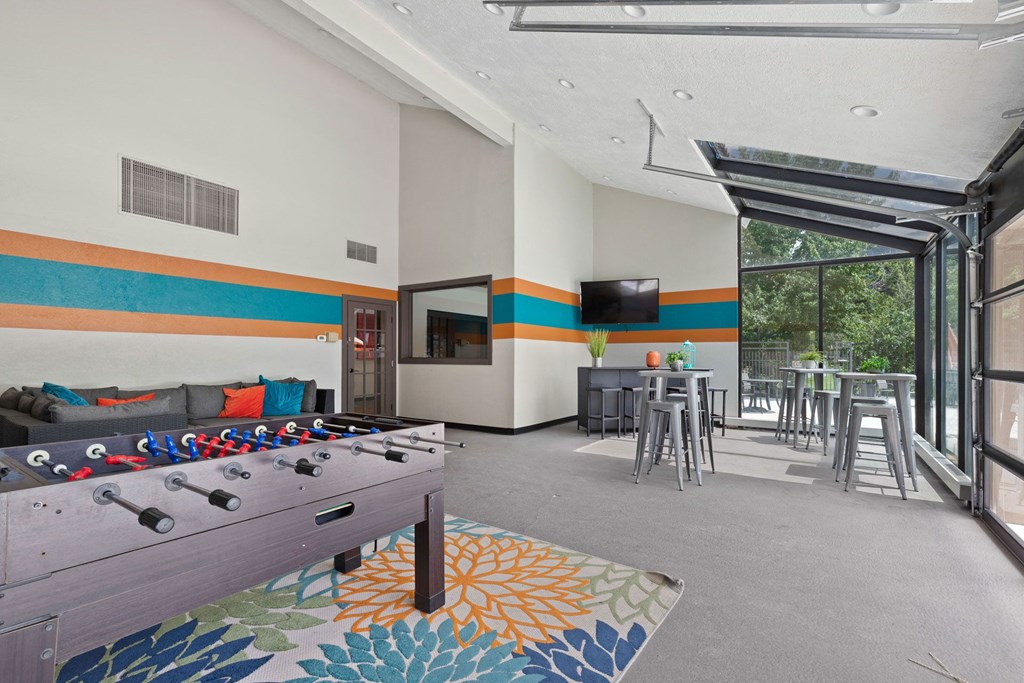 A foosball table is in the middle of a room with a bar and stools.