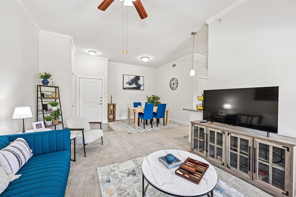 A living room with a blue couch, a television, and a ceiling fan.