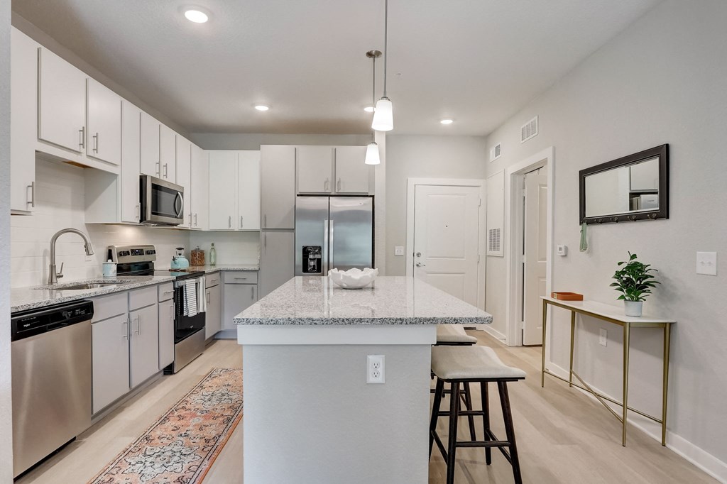 an open kitchen with a large island with granite counter top and stainless steel appliances