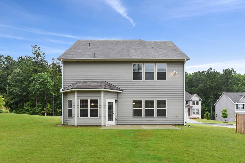 the front of a gray house with a green lawn and trees