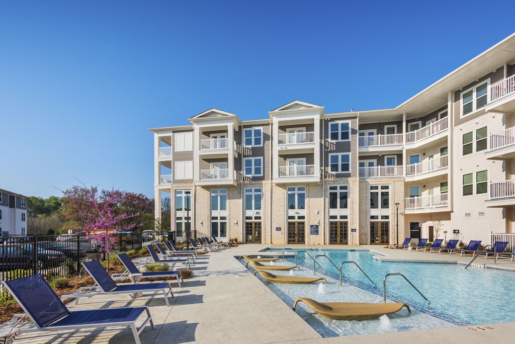 a large swimming pool with lounge chairs in front of an apartment building