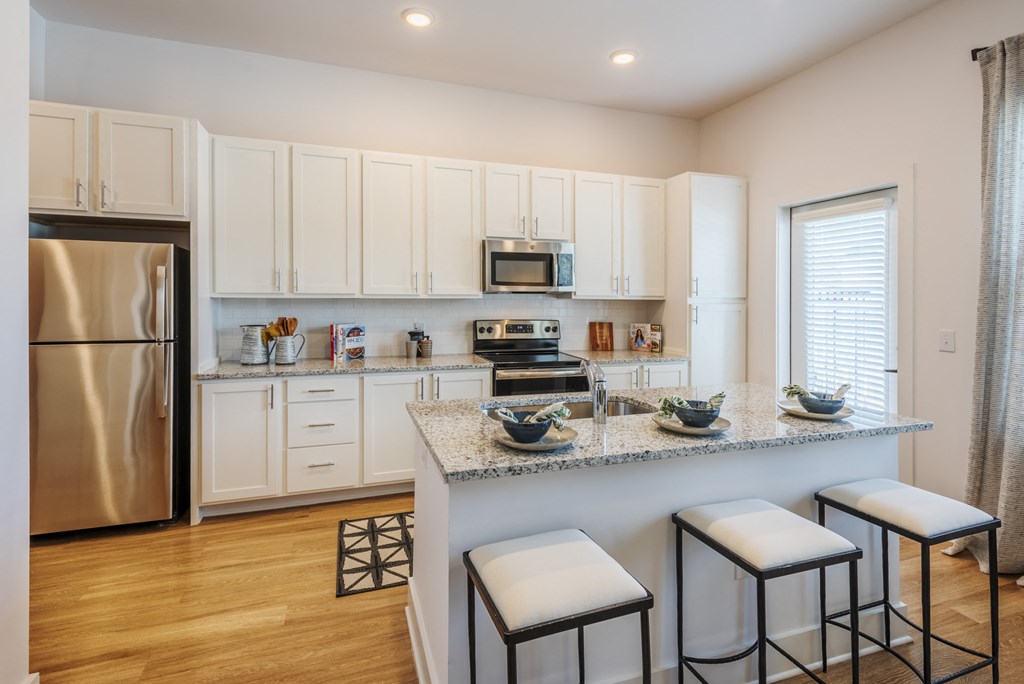 a kitchen with white cabinets and a counter top with three stools
