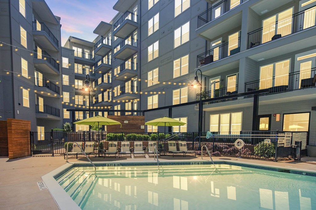 a swimming pool with tables and umbrellas in front of an apartment building