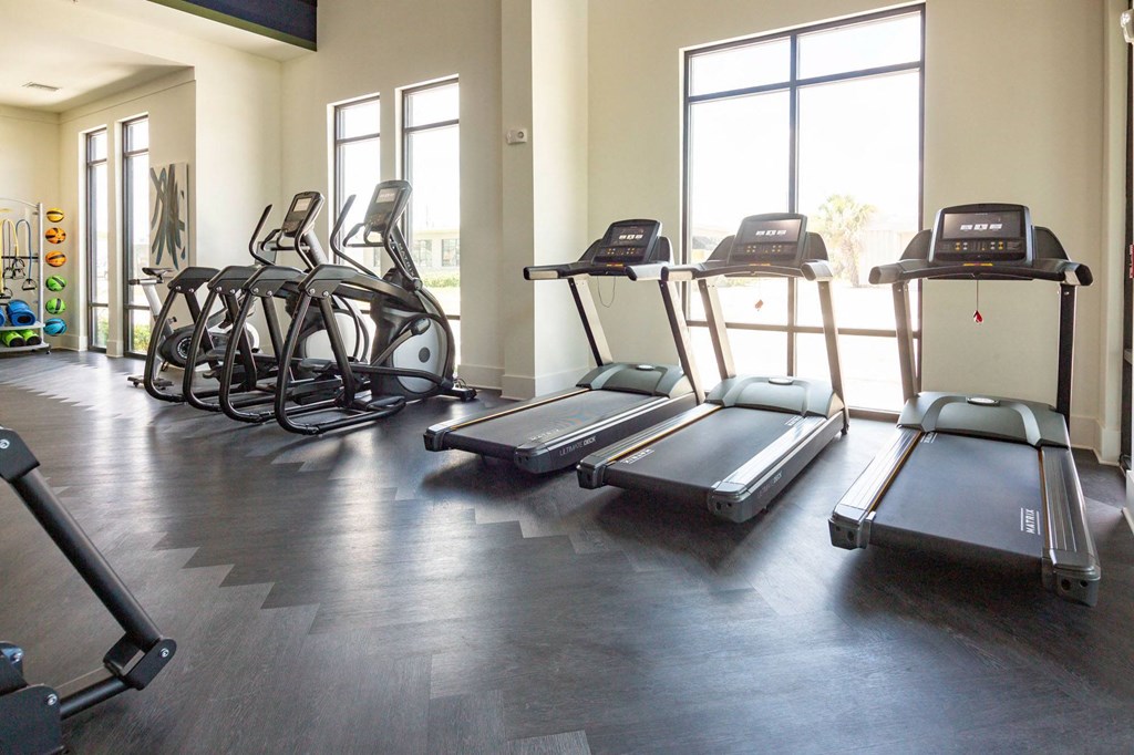 a workout room with cardio equipment and windows in a building