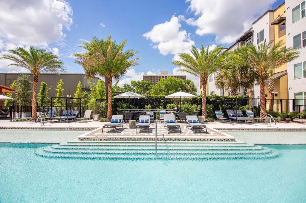 a swimming pool with chairs and umbrellas in front of a building