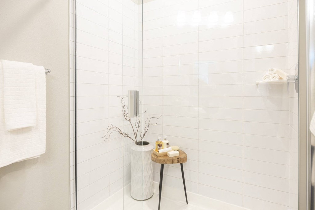 a white tiled bathroom with a shower and a small stool