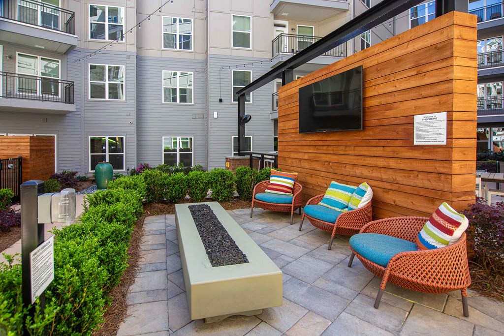 a patio with chairs and a fire pit in front of an apartment building