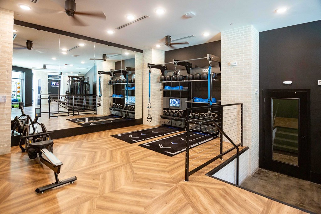 a gym with a wood floor and a mirrored wall with weights and racks