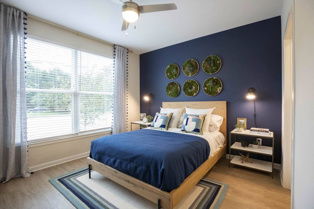 1-BR Apartments in Atlanta, GA - Live 8 West - Bedroom with Blue Accent Wall, Hardwood-Style Floors, Large Window, and Ceiling Fan