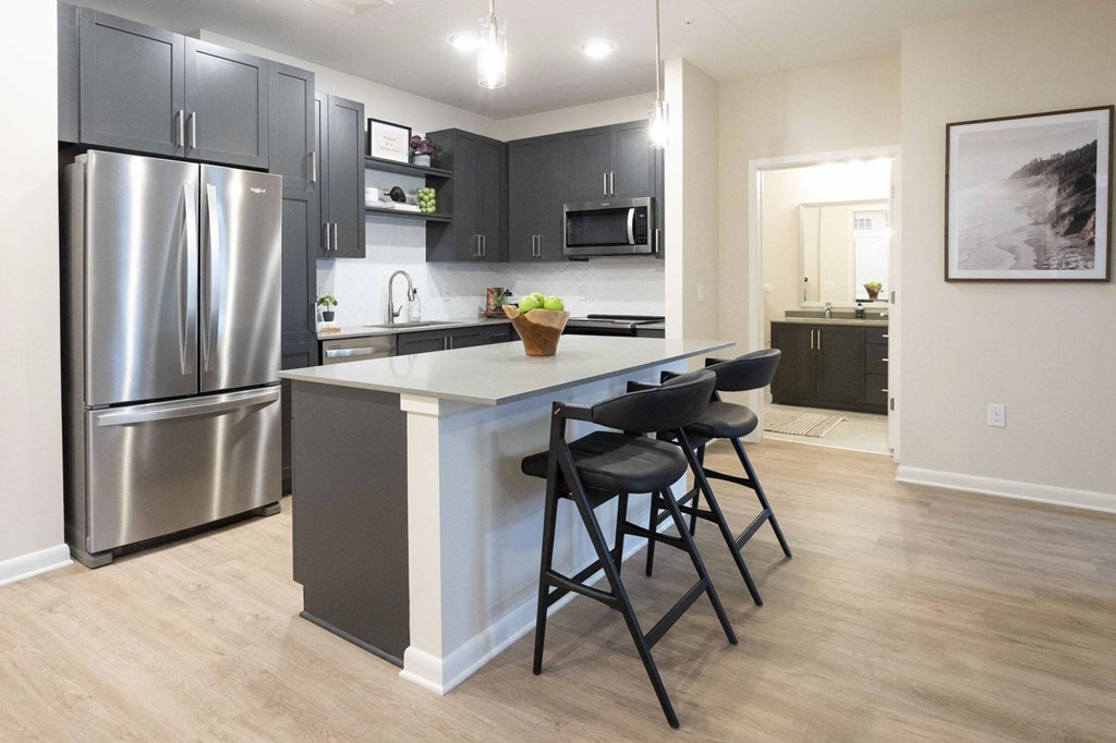 Atlanta, GA Luxury Apartments - Live 8 West - Open-Concept Kitchen with Grey Cabinetry, Stainless Steel Appliances, Light Grey Countertops, Large Center Island with Seating, Light Hardwood-Style Flooring, and Storage Shelves