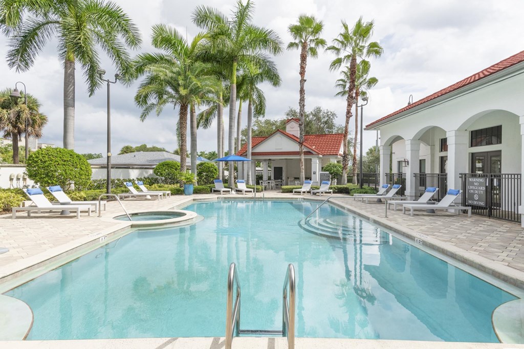 a large swimming pool with chairs and palm trees