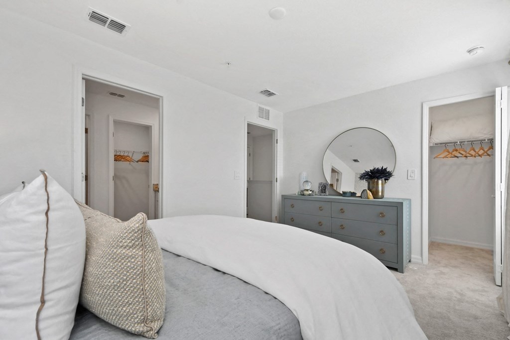 a white bedroom with a bed and a dresser with a mirror