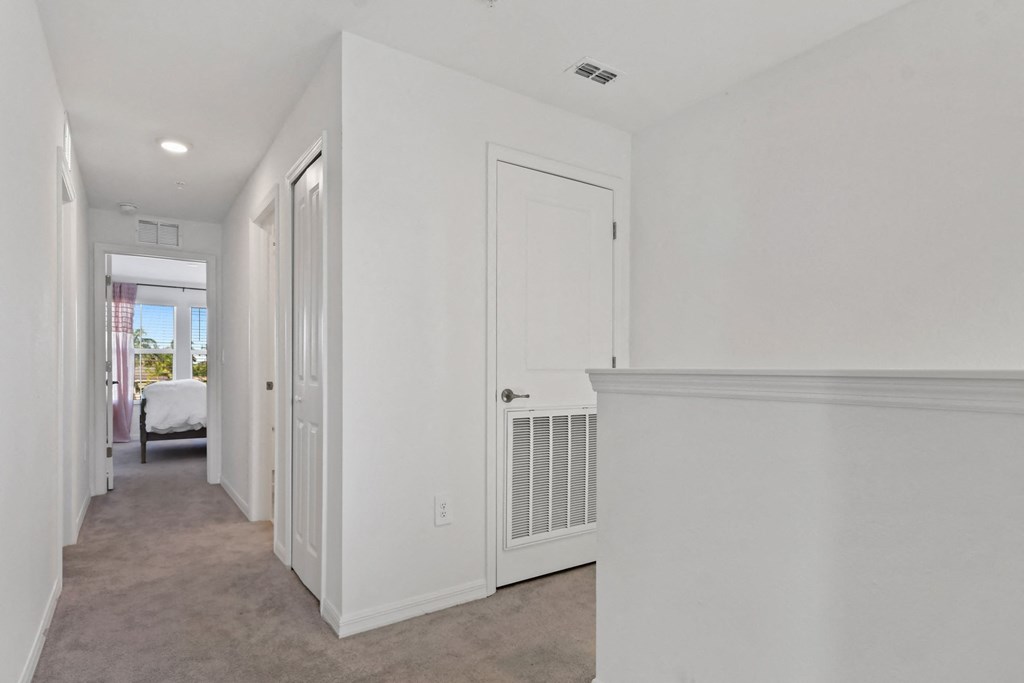 an empty hallway with white walls and white doorways and a bedroom with a bed