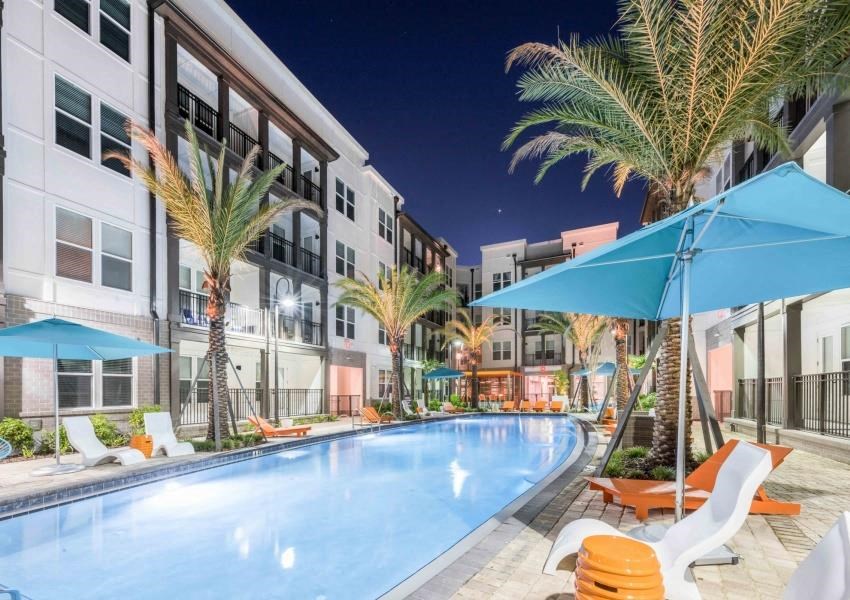 a swimming pool with chairs and umbrellas at night
