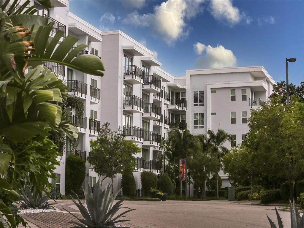 a large white apartment building with trees and a road