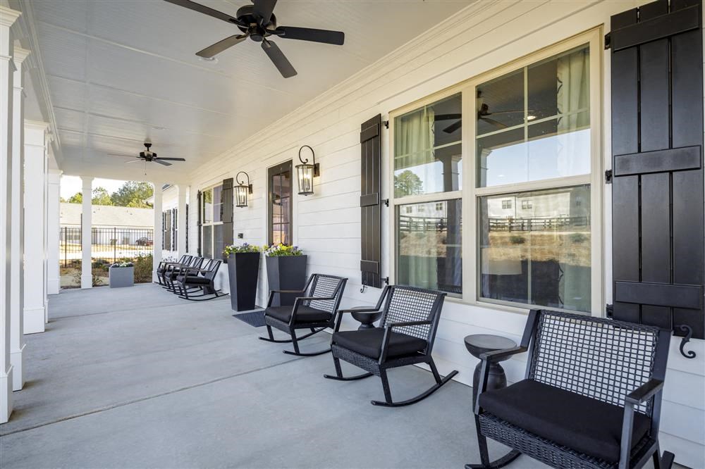 the front porch of a home with rocking chairs and a ceiling fan