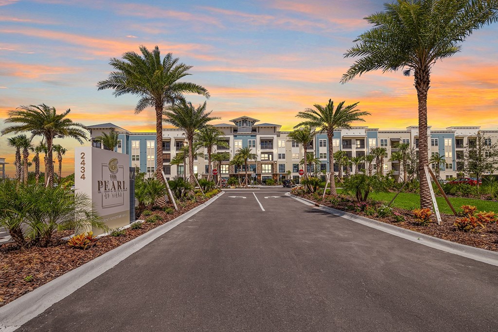 an empty parking lot with palm trees in front of apartment buildings