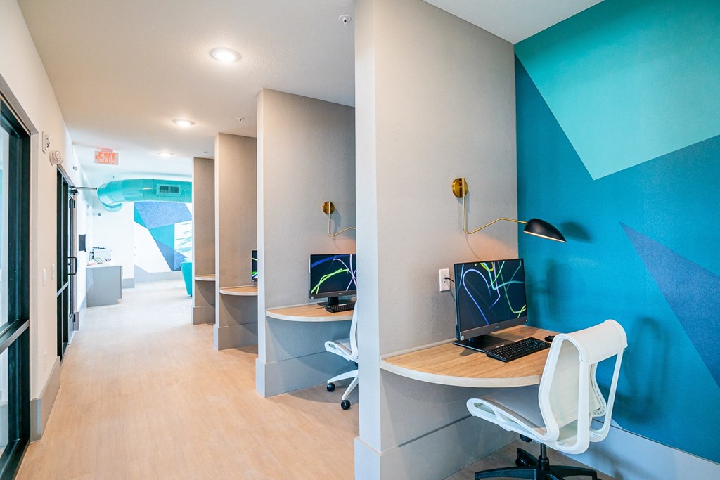 a room with a desk with a computer on it and a blue wall