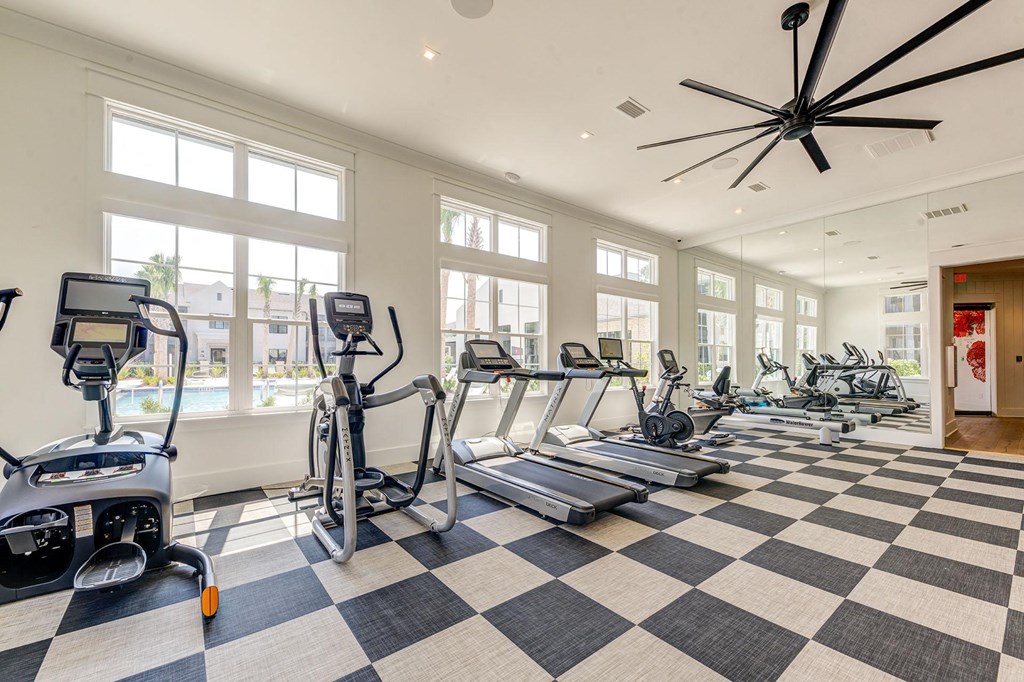 a gym with cardio equipment and large windows