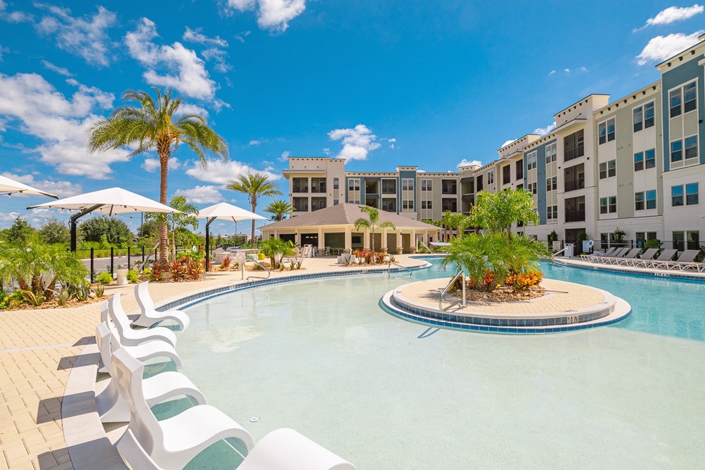 a large swimming pool with chairs and umbrellas in front of an apartment building