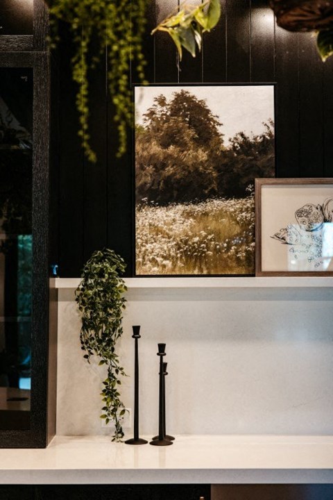 a white counter with a plant and a picture on the wall