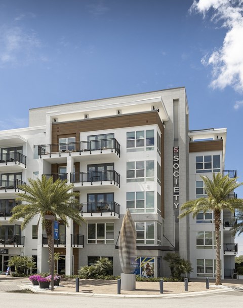 A modern apartment building named "Society" with balconies and palm trees in front.