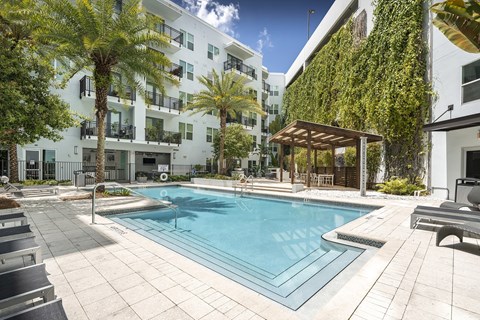 A pool surrounded by palm trees and a building with a green wall.