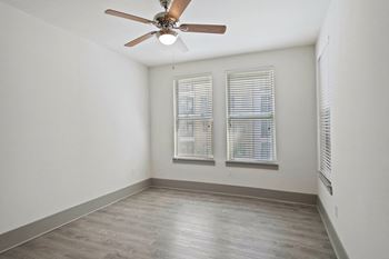 an empty room with a ceiling fan and two windows
