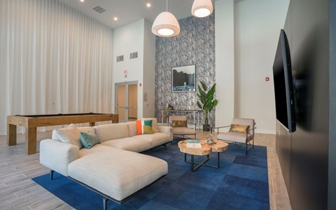 A living room with a blue rug and a television on the wall.