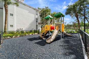 a playground with two slides and two umbrellas in front of a building