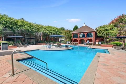 A large swimming pool surrounded by a brick patio and lounge chairs.
