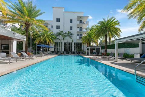 A large swimming pool in front of a white building surrounded by palm trees.