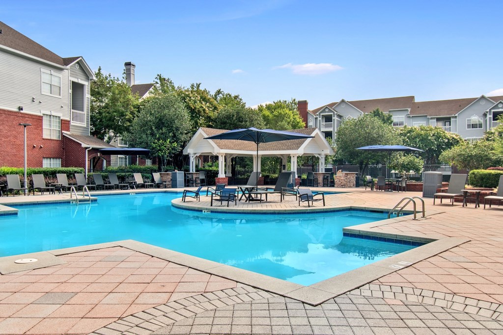 A large swimming pool surrounded by a brick patio and lounge chairs.
