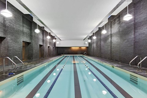 A long indoor swimming pool with a brick wall on the side.
