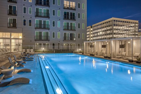 A swimming pool with lounge chairs is surrounded by apartment buildings.