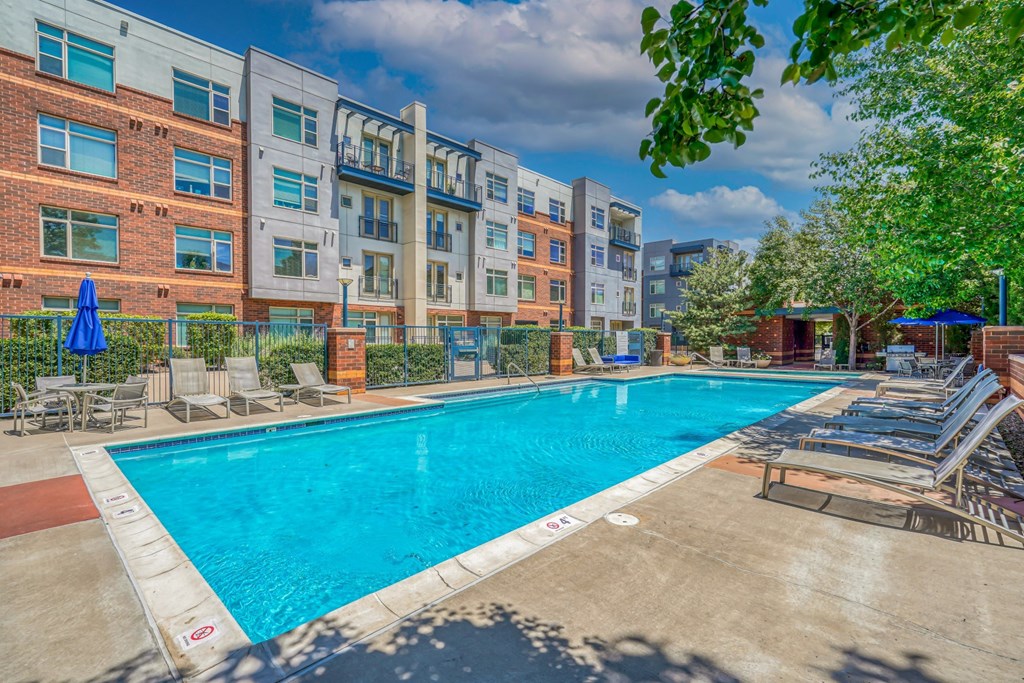 A swimming pool with chaise lounge chairs and a building in the background at The District, Denver, CO