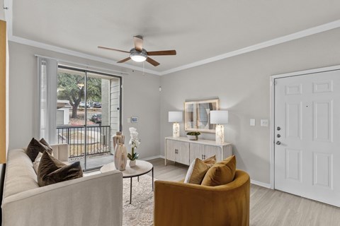 A living room with a white couch, a brown armchair, a glass table, and a ceiling fan.