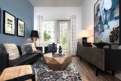 A living room with a black couch, a wooden coffee table, and a large painting on the wall.