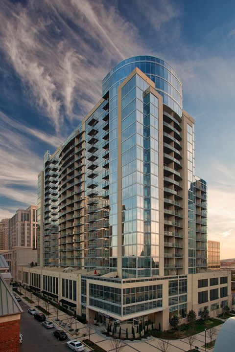 A modern glass building with a curved facade stands tall against a partly cloudy sky.