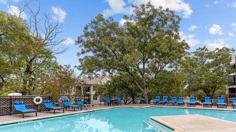 A pool surrounded by trees and chairs.