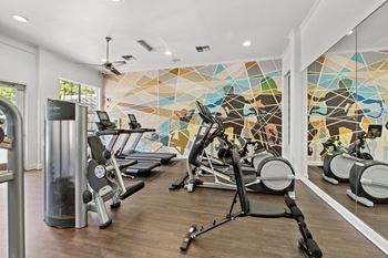 a gym with cardio equipment and a colorful wall mural