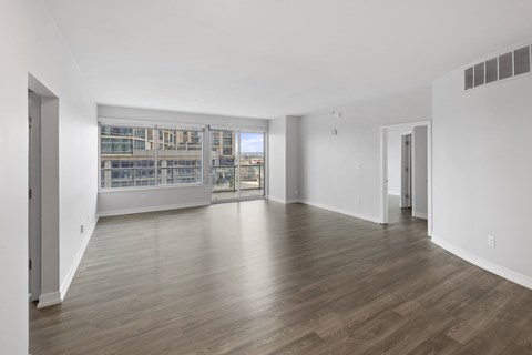 A spacious room with wooden flooring and a view of a building through the windows.