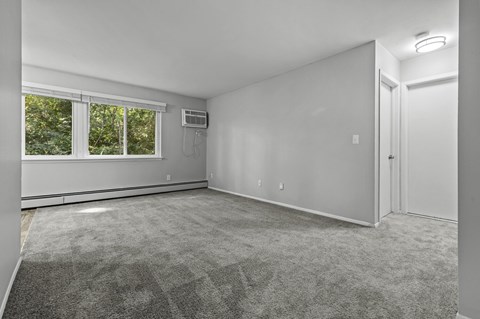 A spacious room with a carpeted floor and a window with blinds.