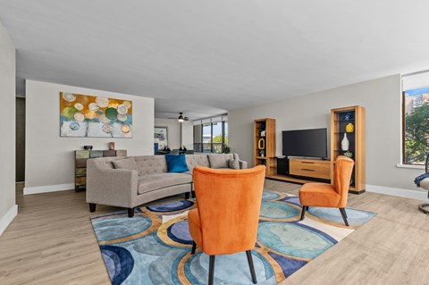 A living room with a grey couch, orange chairs and a painting on the wall.