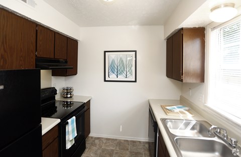 A kitchen with a black refrigerator, a white oven, a white sink and brown cabinets.