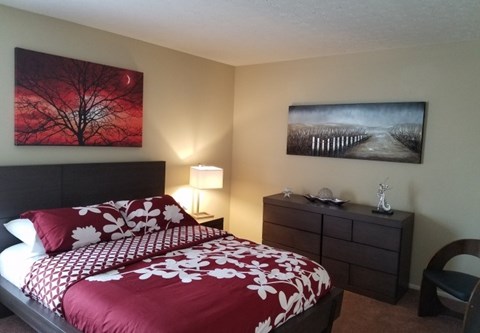 A bedroom with a red and white bedspread and a painting on the wall.