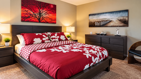 A bedroom with a red and white bedspread and two lamps on either side of the bed.