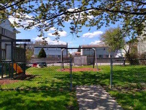 A playground with a swing set and a slide is surrounded by a fence and trees.