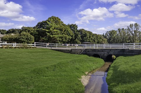 A bridge over a stream in a grassy field.