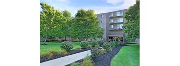 a sidewalk in front of an apartment building with grass and trees